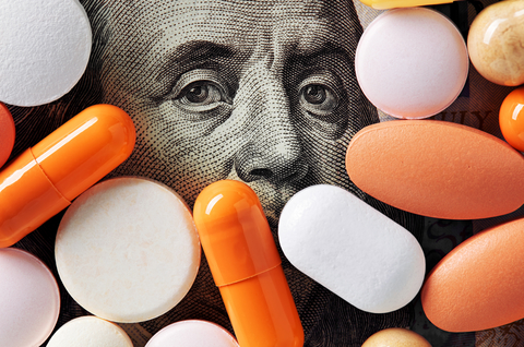Money and healthcare policy concept. Colorful medical pills cover Benjamin Franklin's face on one hundred american dollar bill. Macro top down view. Pharma cash
