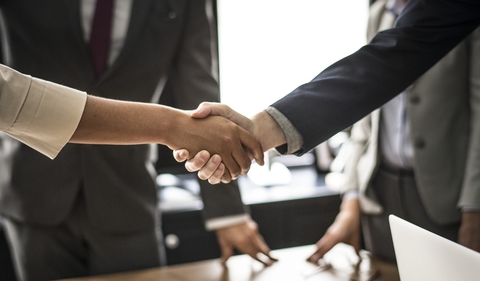 handshake Close-up of two people shaking hands with other people in the background