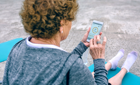 Older woman using smartphone A senior woman sitting on a yoga mat looks at a smartphone with information about heart rate.