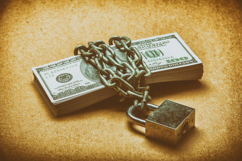 Stack of money protected by a lock and chain Lock and chain securing stack of cash