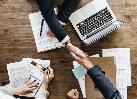 Handshake over desk People shaking hands across a desk that has computer and papers on it