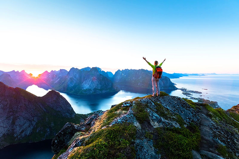 Solo Travel Getty Happy woman hiker enjoying scenic view of midnight sun at the top of Reinebringen hike above Reine village in the Lofoten archipelago during arctic summer, Norway