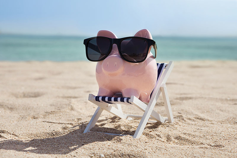 Summer Savings Vacation Beach Piggy Bank Getty Piggy bank wearing sunglasses on a beach