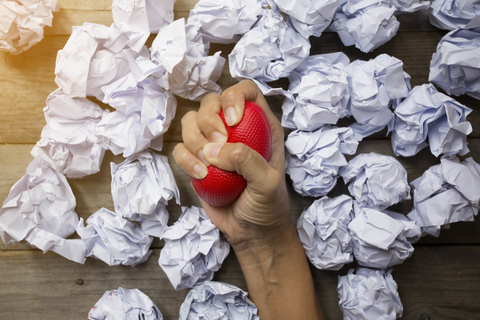 Woman's hand squeezing stress ball surrounded by crumpled paper Stress ball squeezing surrounded by crumpled paper