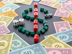 Monopoly money, cars, dice, hotels A dollar sign created by Monopoly game houses is surrounded by Monopoly money. Dice and the car token appear next to the dollar sign as well.