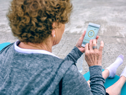 Older woman using smartphone A senior woman sitting on a yoga mat looks at a smartphone with information about heart rate.