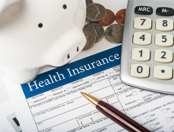 Paying for health insurance Health insurance form with wood pen, basic calculator, white piggy bank, and pile of coins