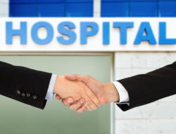 Hospital merger Photo of two men shaking hands in front of a hospital