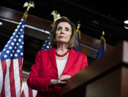 Nancy Pelosi An image of Nancy Pelosi standing at a podium wearing a red blazer.