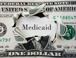 Medicaid spending Dollar bill with a hole in Washington's face on it and the word "Medicaid" in its place