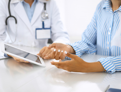 patient engagement and doctor with tablet Doctor and patient talking and discussing health treatment while sitting at the desk. Physician pointing into tablet pc.