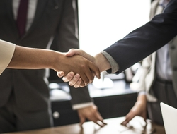 handshake Close-up of two people shaking hands with other people in the background