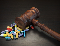 Drug lawsuit Wooden gavel over small pile of multi-colored pills on dark background.